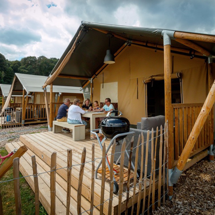 luxe tent met een terras en barbecue ervoor, waar het hele gezin bij elkaar zit. 