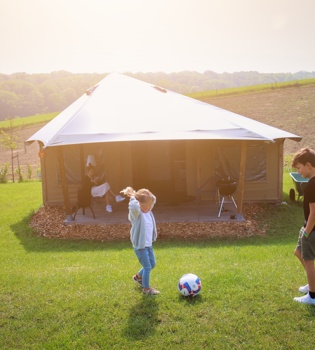 Kinderen zijn aan het voetballen voor de luxe tent in een natuurrijke omgeving. 