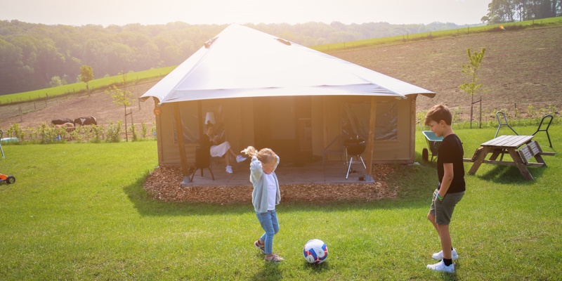 Kinderen zijn aan het voetballen voor de luxe tent in een natuurrijke omgeving. 