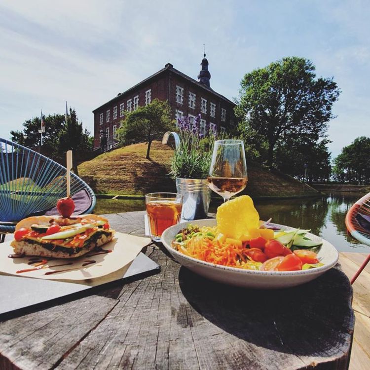 Lunchgerechten en drankjes op een houten tafel met uitzicht op Kasteel Limbricht