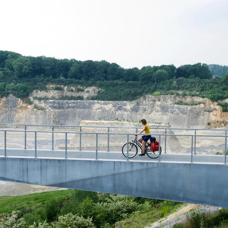 Een vrouw fietst over een ijzeren brug bij de ENCI groeve