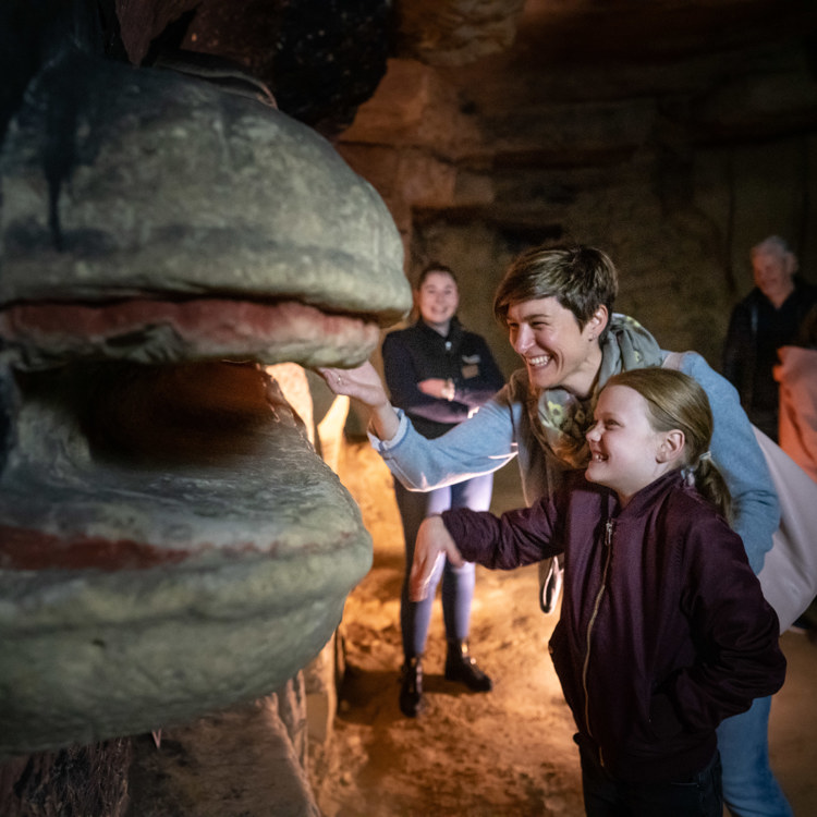 Vrouw met kindje raken een mergelsculptuur aan tijdens rondleiding Fluweelengrot