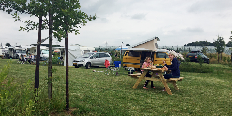 Gezin zit aan picknicktafel op de camping. 