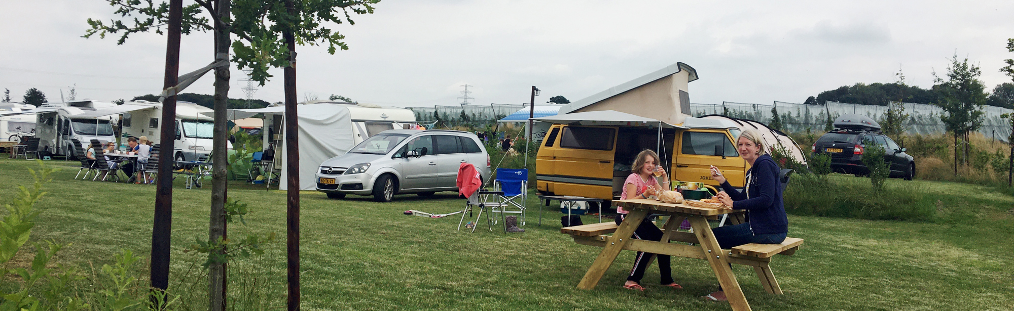 Gezin zit aan picknicktafel op de camping. 