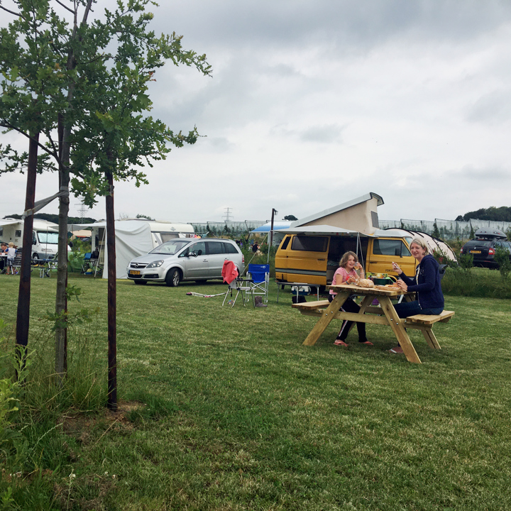 Gezin zit aan picknicktafel op de camping. 