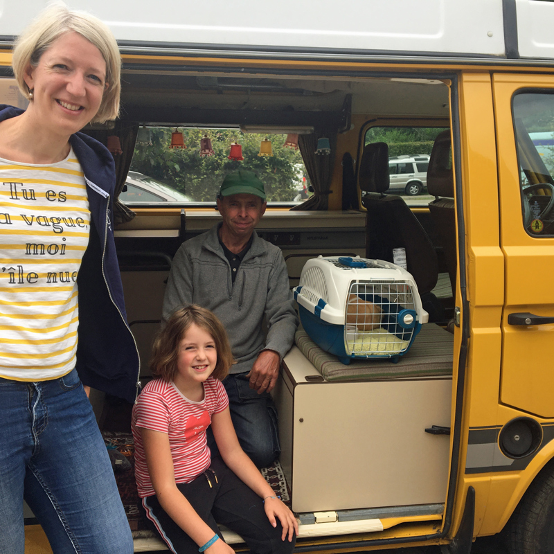 man vrouw en dochter poseren in de opening van een geel camperbusje. 