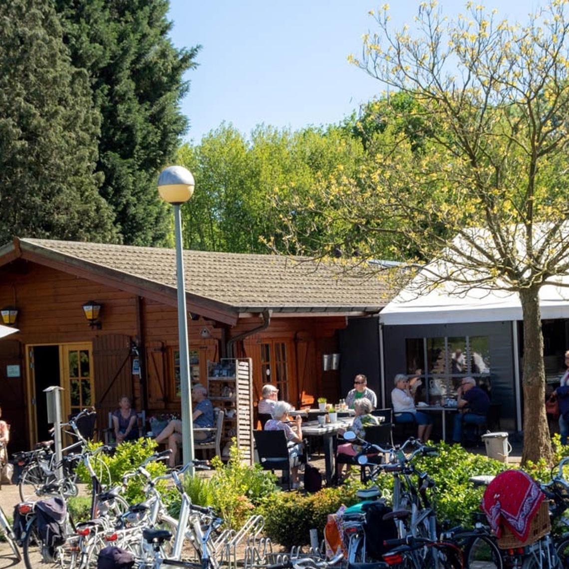 Een druk terras vol met tafeltjes, mensen, fietsen bij Koffiehuis het Ijzerenbos