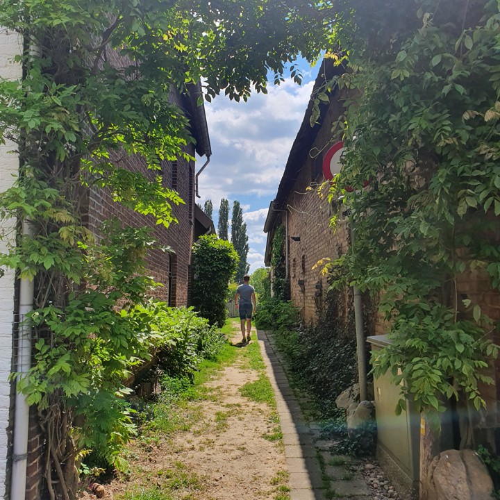 Een jongeman wandelt tussen twee huizen door over een wandelpad naar het Vrouwenbos