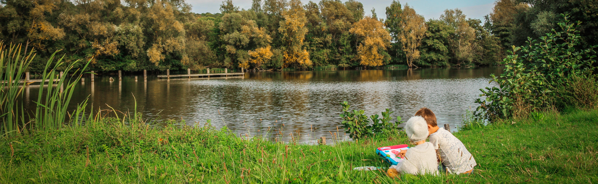 Kinderen lezen een kaart in het grasveld bij een meer omringt door herfstbomen