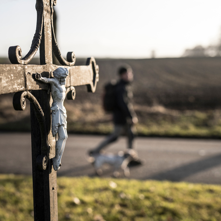 Man met hond loopt langs een wegkruis