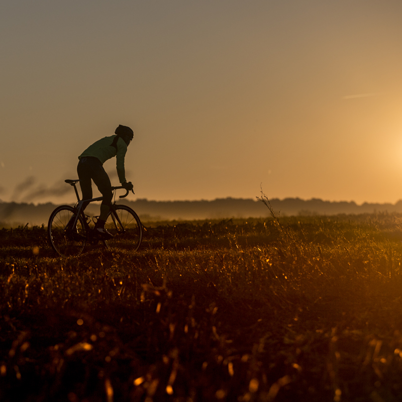 Wielrenner fietst een heuvel op met zonsondergang