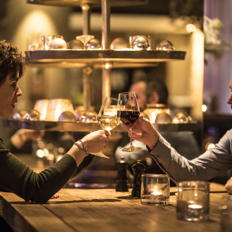 Een koppel proost met wijn en kerstverlichting op de achtergrond