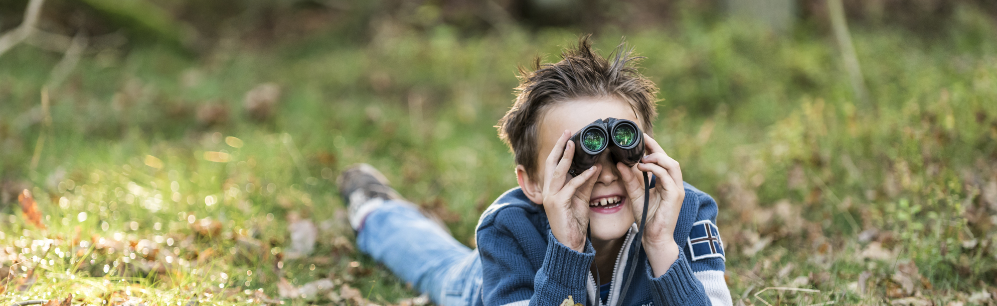 Een jongen die in het gras ligt en door een verrekijker kijkt