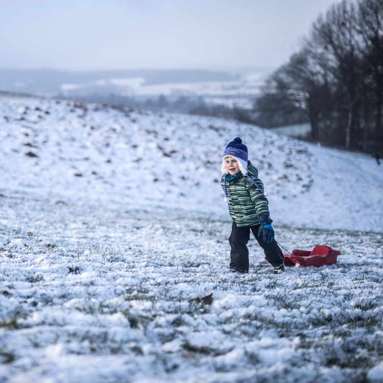 Jongetje met slee in winterkleding loopt de besneeuwde berg op