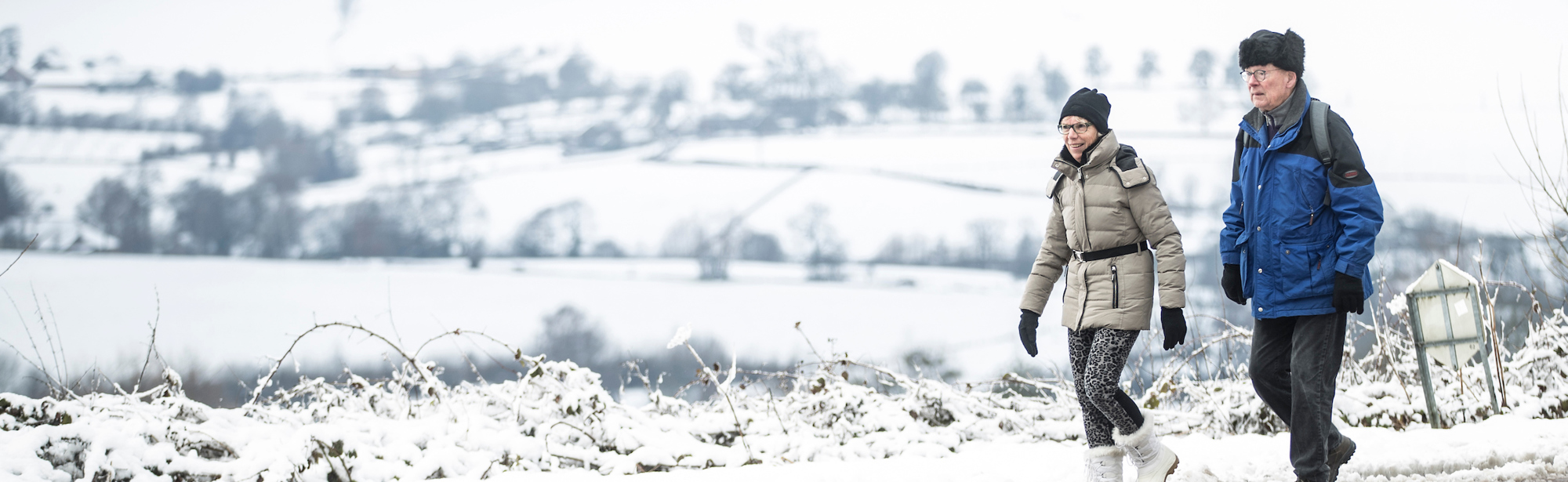 Twee wandelaars wandelen in een winterwonderlandschap met uitzicht over de witte heuvels