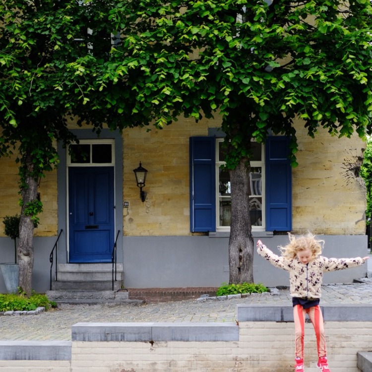 meisje springt van een muurtje af voor een mergelwoning. 