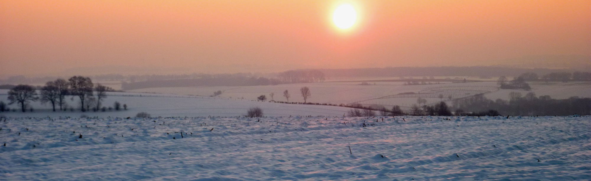 Zonsopkomst over besneeuwd landschap met een roze gele gloed