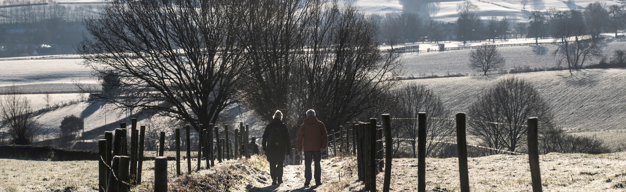 Twee wandelaars lopen een heuvel af in een winters landschap bij Epen