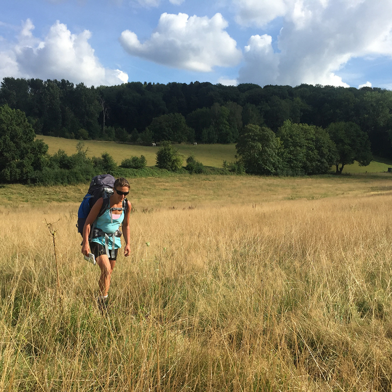 Een vrouw met een backpack wandelt door een veld met hoog gras
