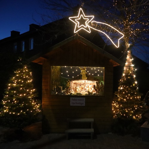 houten huisje met daarin een verlichte kerststal in donker