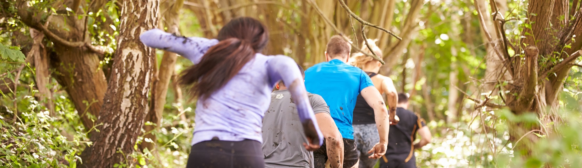 Deelnemers van een trailrun rennen in een rijtje achter elkaar door de modder van het bos