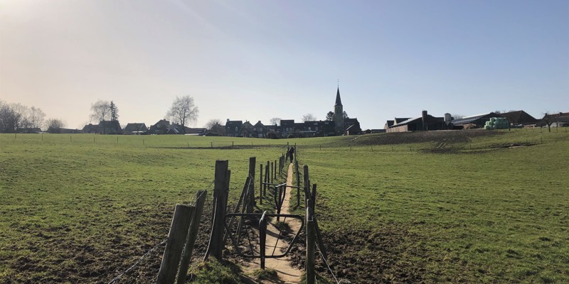 Twee draaihekjes bij een wandelpad door het weiland met op de achtergrond een kerk