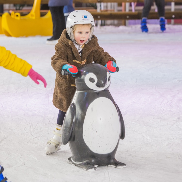 Kindje met helm schaatst met hulp pinguïn