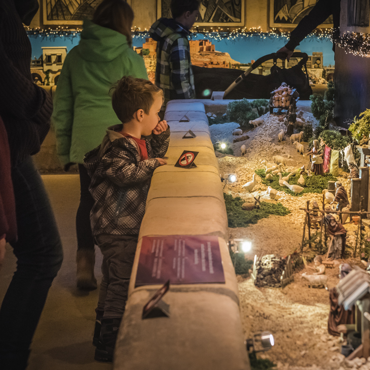 Jongetje leunt over mergelbalustrade om miniiatuur kerstdorp te bekijken