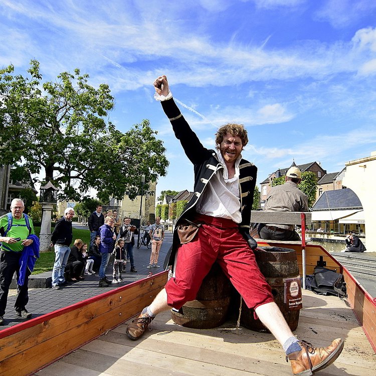 Man in Middeleeuws kostuum zittend op houten vaten houdt vuist in de lucht op kar in Centrum Valkenburg