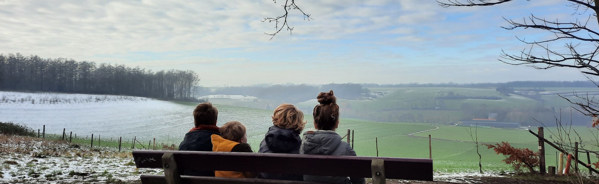 Vier kindjes zitten op een bankje en kijken uit op een winters landschap bij het Gulpdal