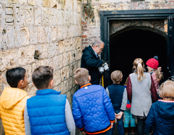 Groepje kinderen vanaf de achterkant en een meneer die uitleg geeft in de grotten. 