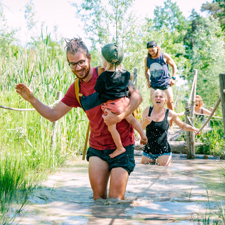 Vader tilt dochtertje over een diepe waterplas bij het blotevoetenpad