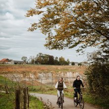 Herfstige setting waarbij een koppel naast elkaar fiets en waarbij je op de achtergrond groeve 't rooth ziet liggen