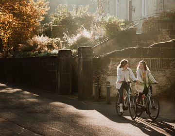 Twee fietsers met op de achtergrond een groot pand van mergel, bomen en een laagstaande zon