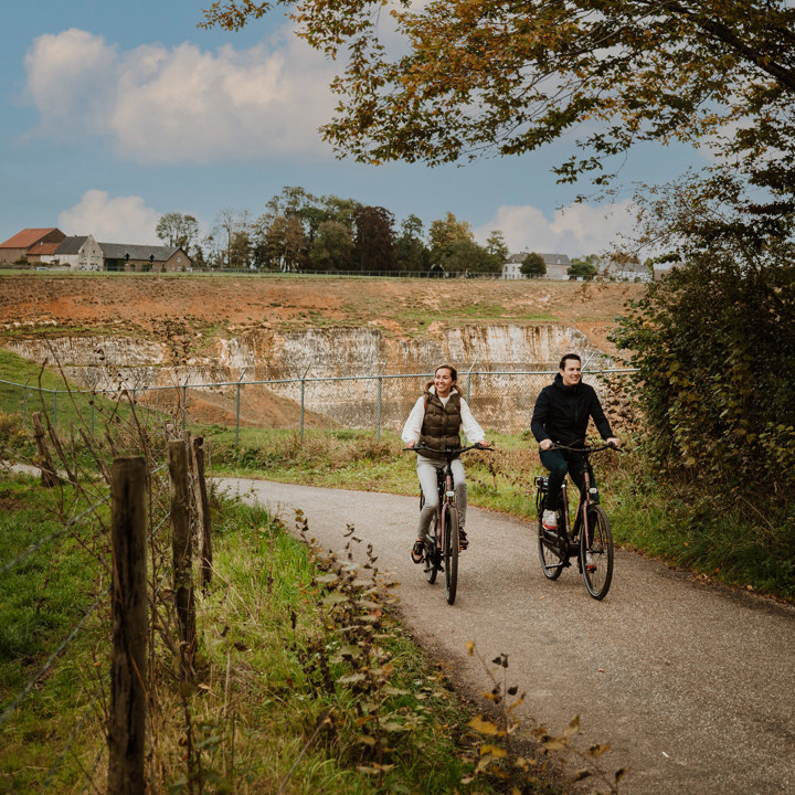 Man en vrouw op de fiets naast elkaar, met mergelgroeve op de achtergrond