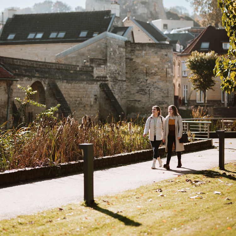 Twee dames lopen door een parkje in Valkenburg met op de achtergrond gebouwen van mergel en steen