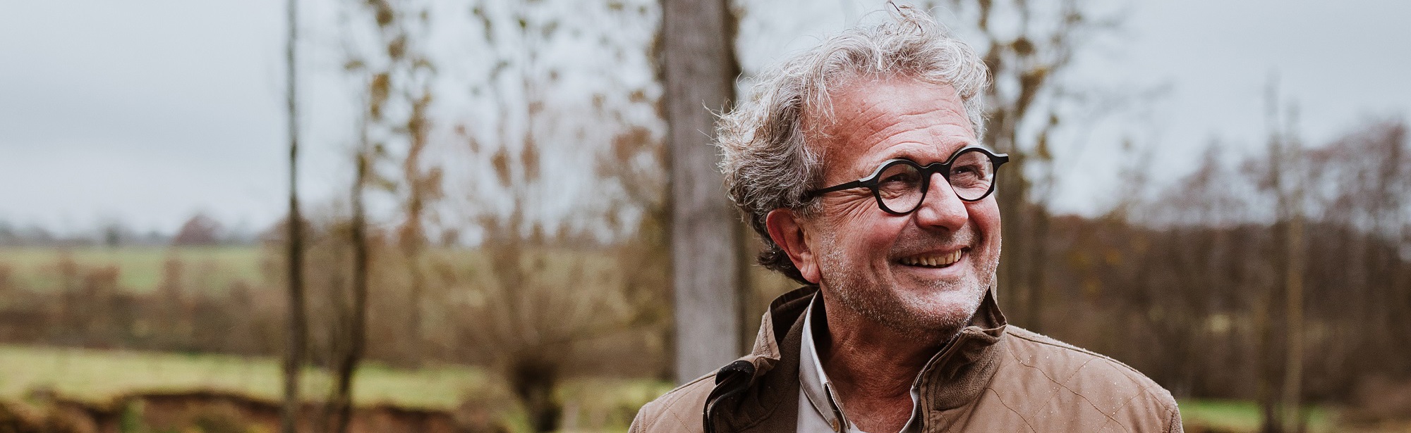 Edmond Staal poseert lachend voor de Geul op een bewolkte dag