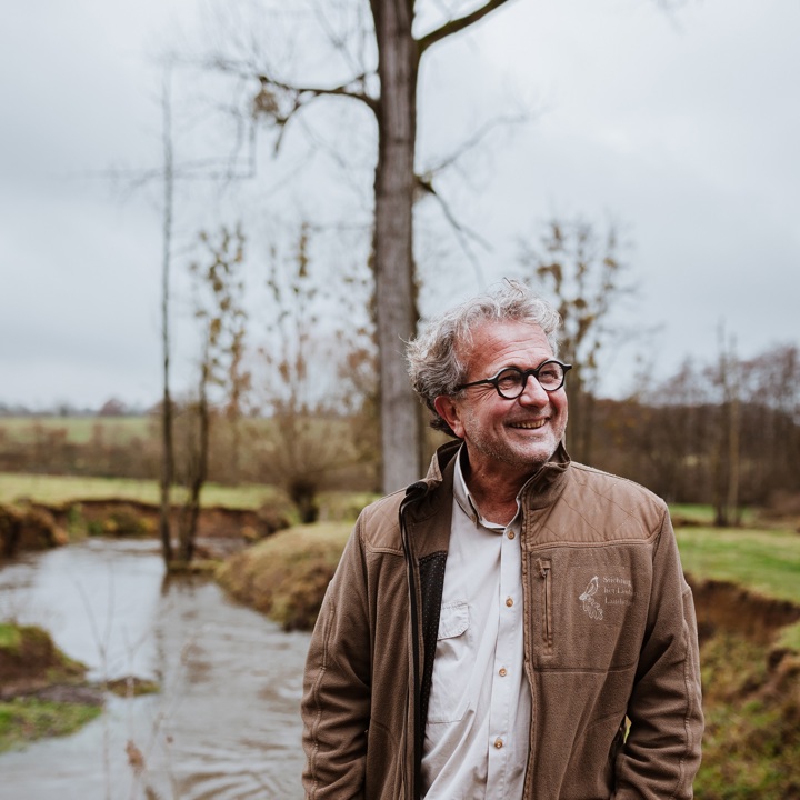 Edmond Staal poseert lachend voor de Geul op een bewolkte dag