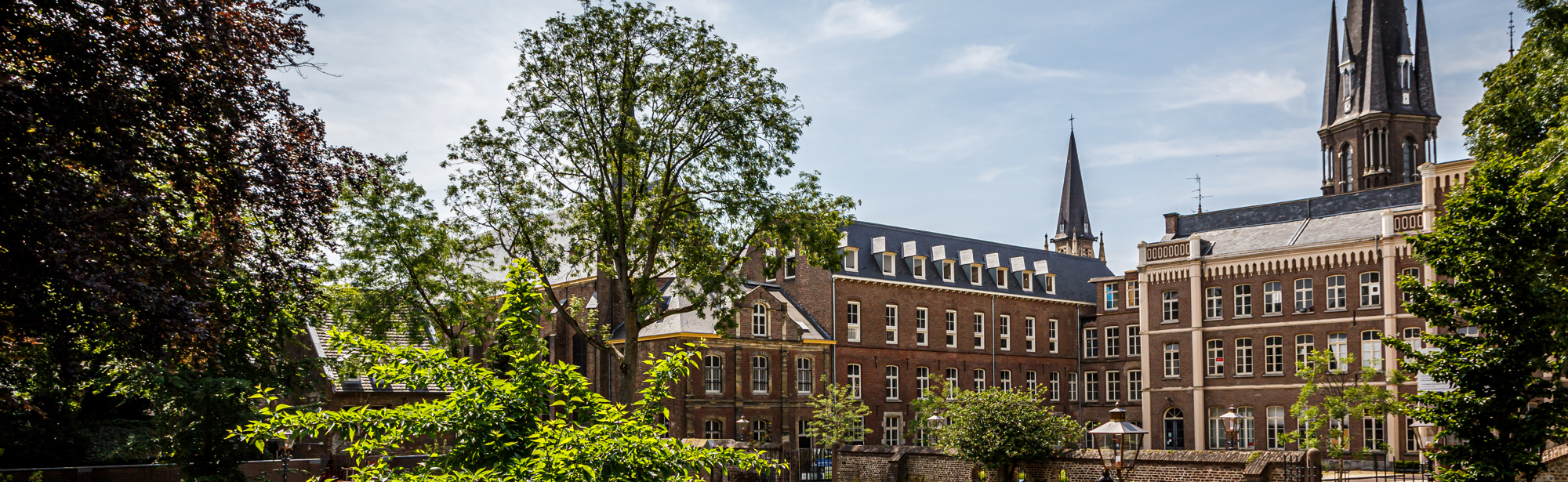 Een ronde tuin met daarachter een indrukwekkend klooster met spitse kerktorens