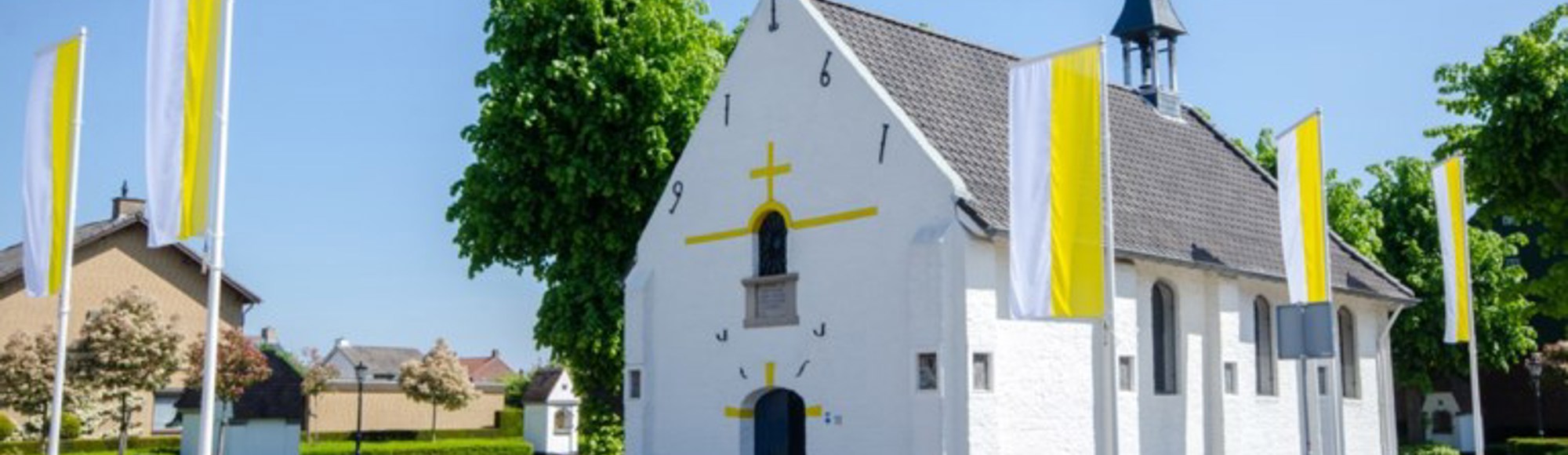 Een witte kapel gelegen aan een straat omringd met witgele vlaggen