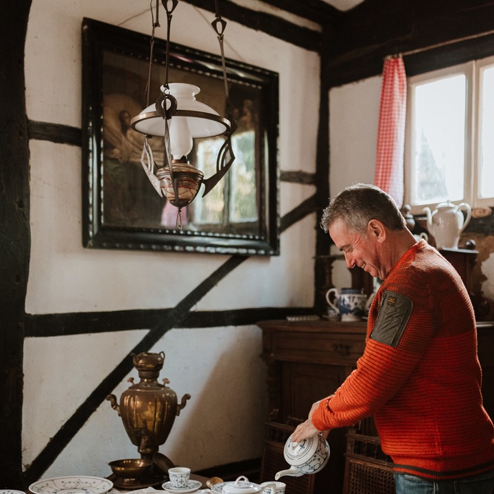 Een meneer schenkt een kopje koffie in een oud Limburgs servies binnen in een vakwerkhuisje