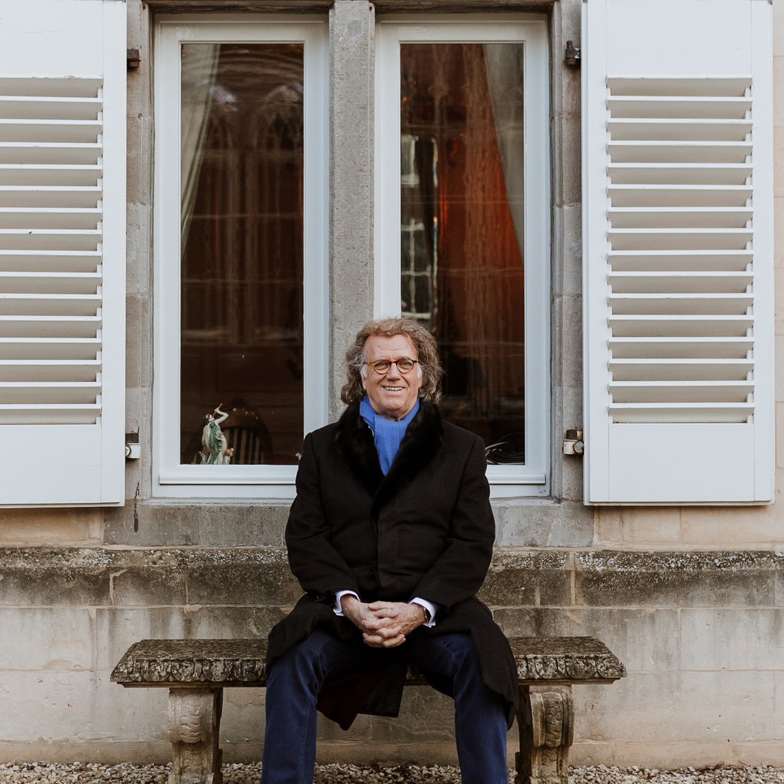 André Rieu poseert op een bankje voor een groot raam met witte luiken