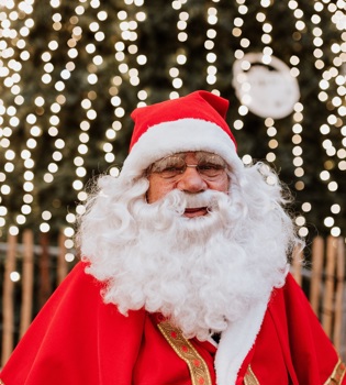 De Kerstman poseert voor een kerstboom vol lichtjes