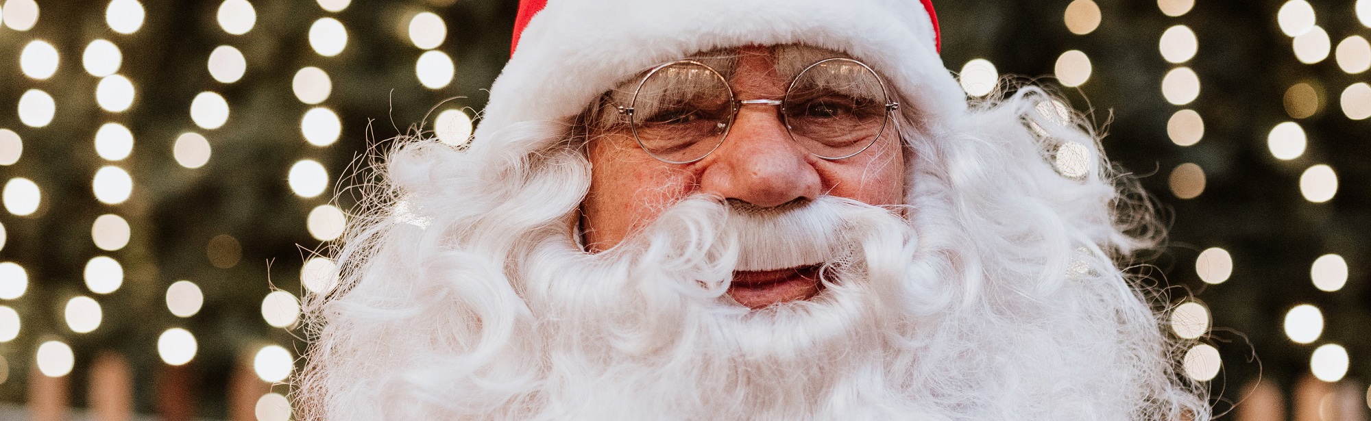 De Kerstman poseert voor een kerstboom vol lichtjes