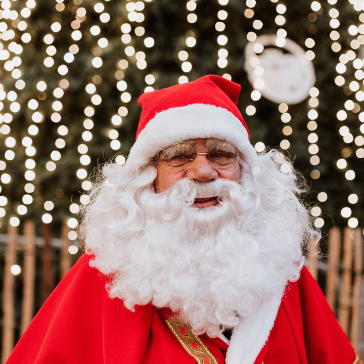 De Kerstman poseert voor een kerstboom vol lichtjes