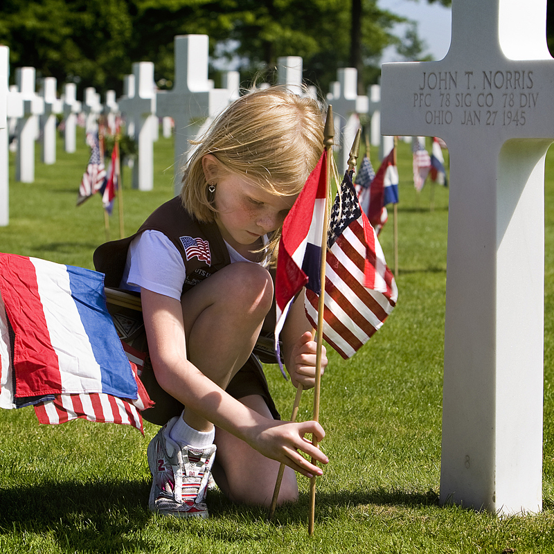 Een meisje plaats een Amerikaanse vlag bij een gedenkkruis op de begraafplaats in Margraten