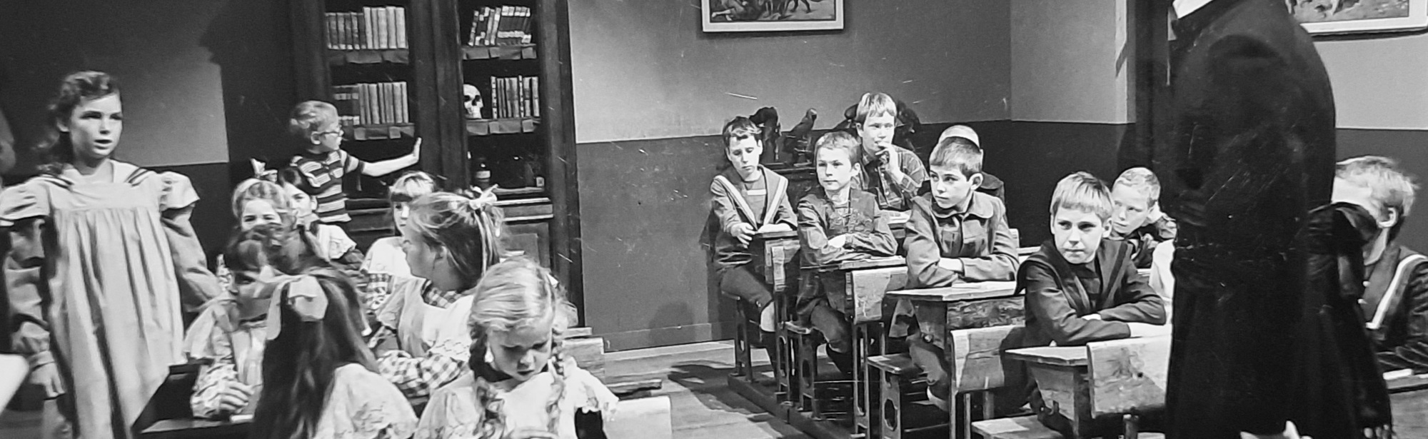 Oude zwart wit foto van Kapelaan Odekerken met kinderen in schoolbankjes in een klaslokaal (Dagboek van een Herdershond)