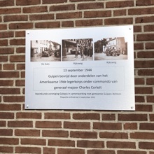 Aluminium plaquette tegen een stenen muur met foto's en tekst over de bevrijding van Gulpen