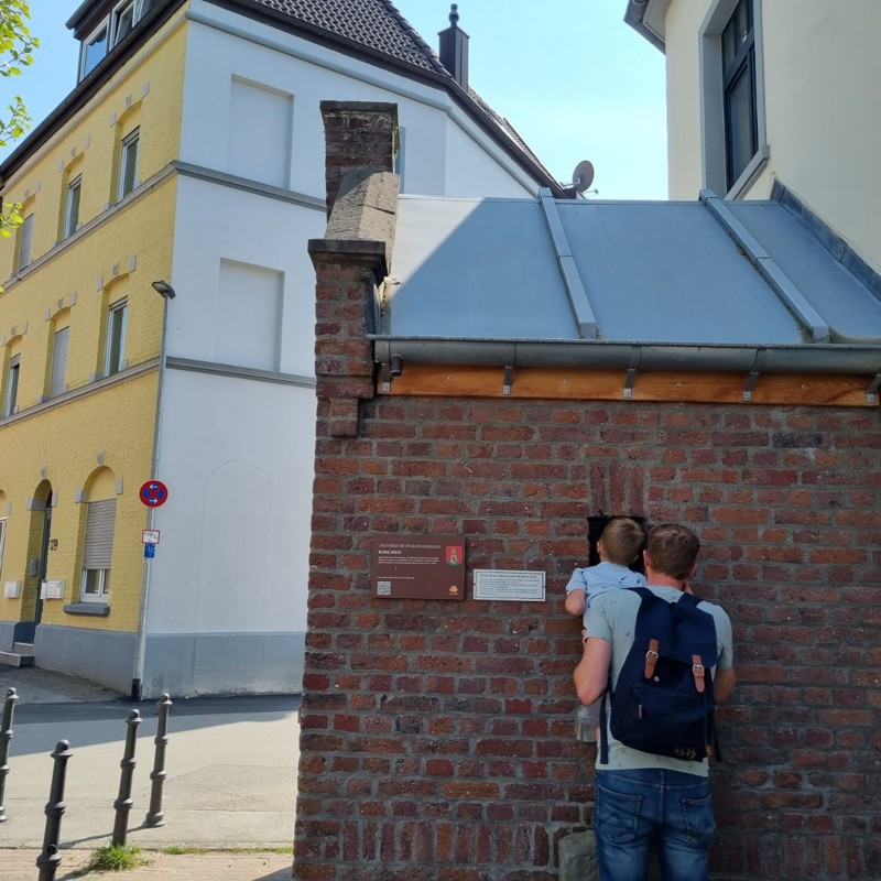 Vader en kindje kijken door een raam in een muur