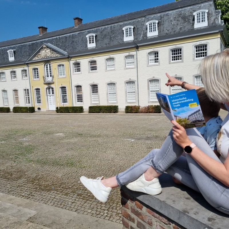 Een vrouw die het routeboekje van Historische stadswandeling Vaals bekijkt en wijst naar een gebouw